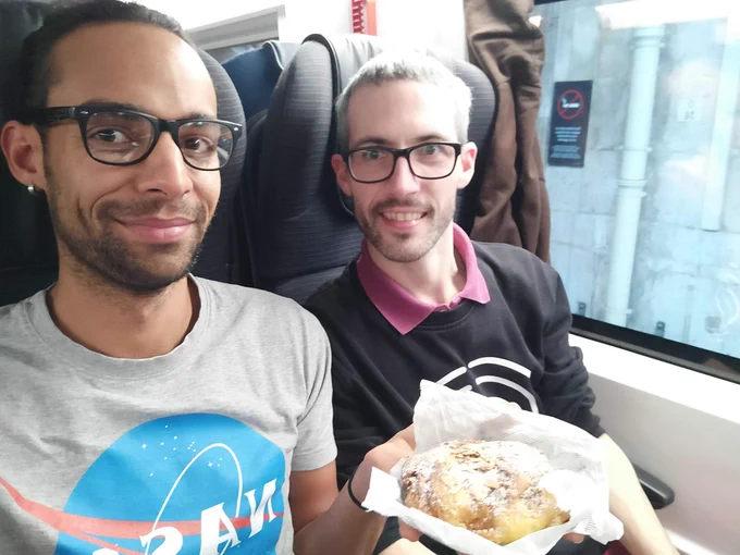 Two people sitting in a train, one holding a croissant