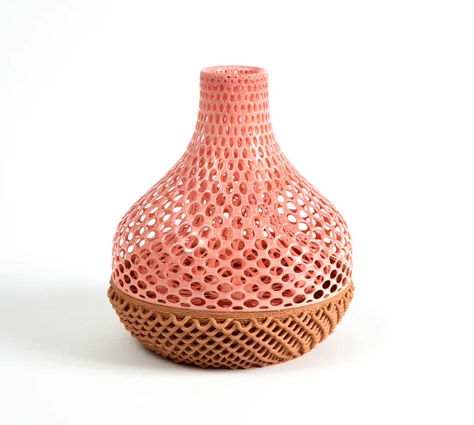 This is a crazy vessel. The form is heavy at the bottom, and narrows at the top. The top 2/3 of the vessel is a pale pink color. It has many circular holes. The bottom of the vessel is taupe. It is composed of loops.