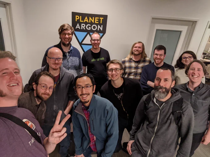 Smiling Rubyists crowded around a PlanetArgon sign.