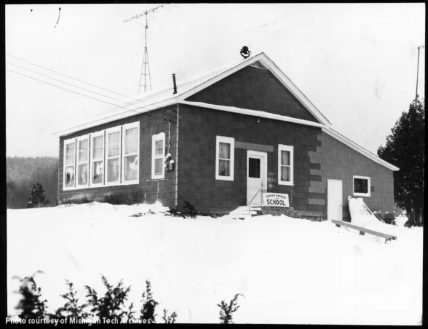 View of rough-sided one-room schoolhouse with radio tower, surrounded by snow