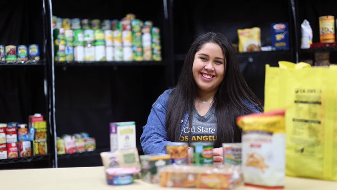 A smiling student in a Cal State LA tee sits inside of food pantry