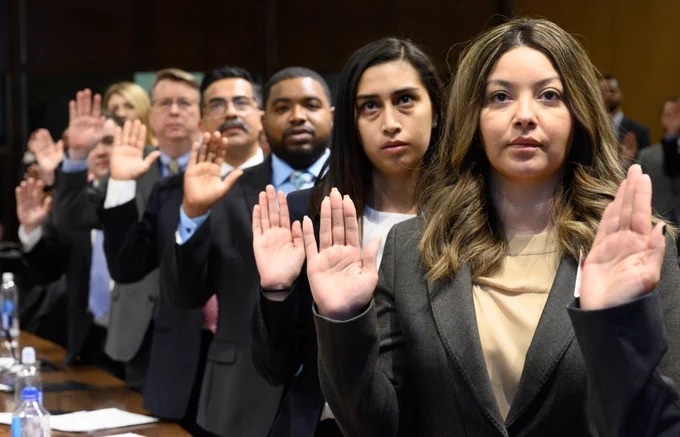 Group of people in suits standing indoors and raising right hand