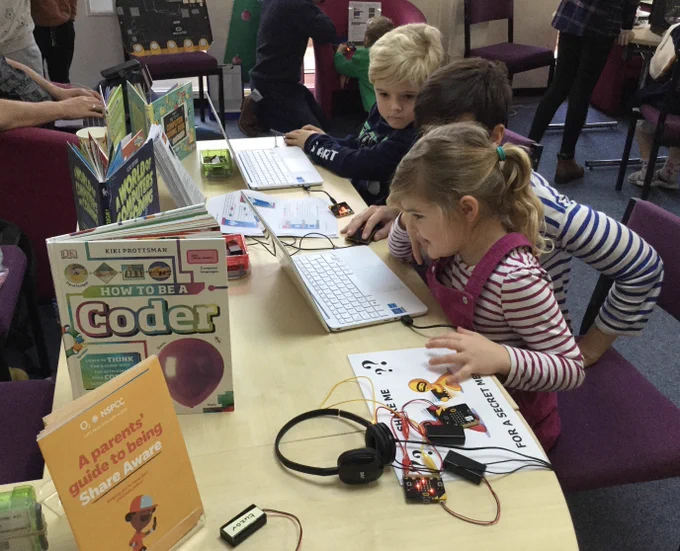 Two children learning to code on laptops with micro:bits, supported by member of staff