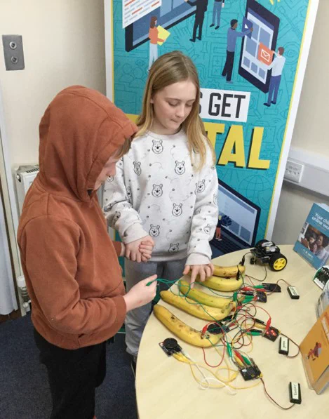 Brother and sister holding hands to complete a circuit in order to play the musical bananas