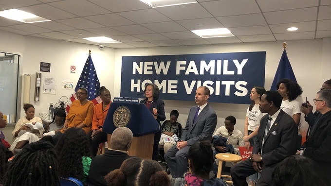 Commissioner Barbot at the podium of a press conference. Behind her, the banner reads NEW FAMILY HOME VISITS