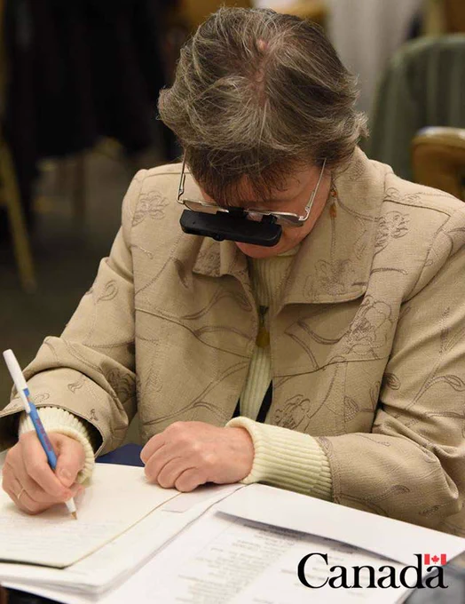 Photo of a woman with glasses, writing on a piece of paper.