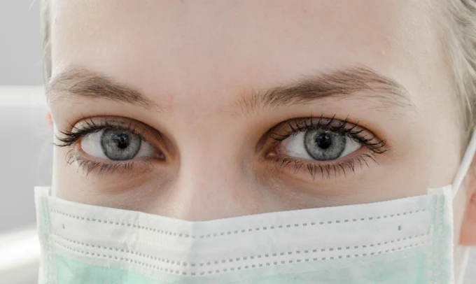 A zoomed in photo of a woman with blue eyes wearing a health face mask.