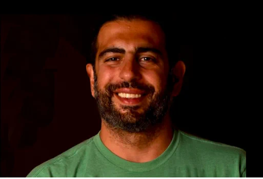 Researcher Foad Hamidi, wearing a green shirt,  smiles at the camera behind a black background