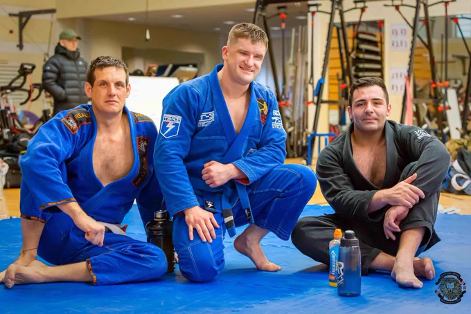 Three men in jiujitsu Gi’s kneeling on the warm up mat at the Army Jiujitsu championship. Rob long in the middle