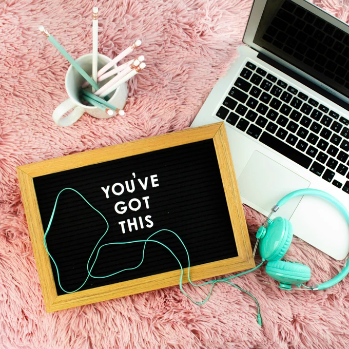 Overhead image of a laptop, headphones, cup with pencils, and marquee board that says "You've got this"
