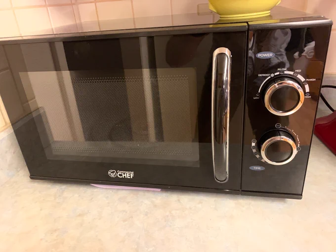 A microwave; glossy black in appearance; with two chrome dials for managing time and power output. 