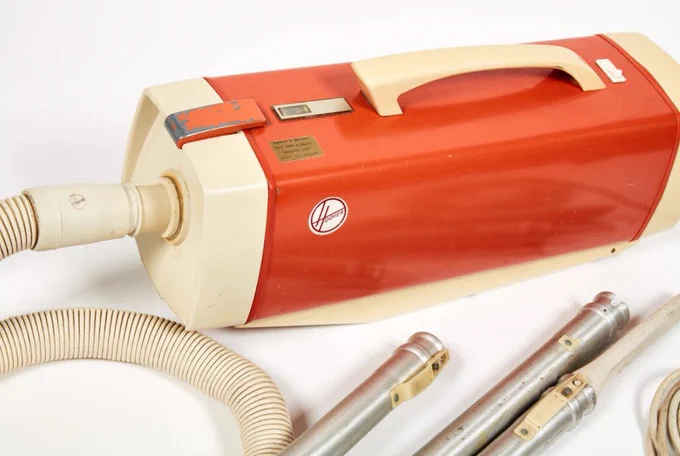 A bright orange and white 1960s cylinder vacuum cleaner with chrome accessories 