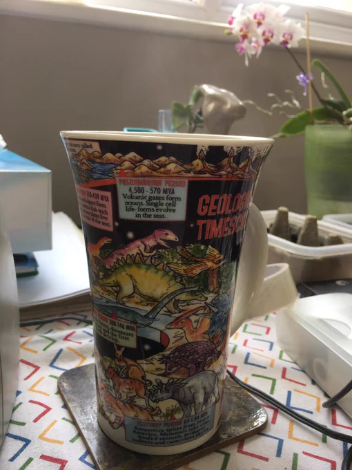 Tall mug with a geological timescale featuring lots of colourful dinosaurs, prehistoric mammals and other animals from the fossil record