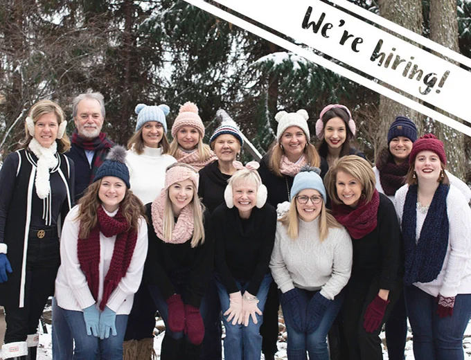 14 people standing outside in snowy landscape, smiling, text on image reads we're hiring