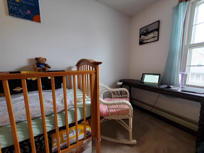 Workspace is in the nursery - we see a crib, teddy bear, and laptop