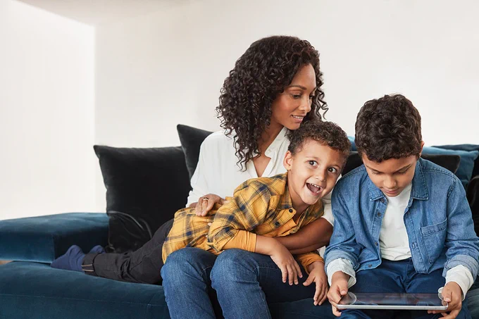 A woman and her two sons sit on a sofa at home and look at a Surface device, suggesting children learning at home