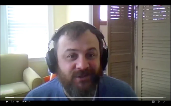 Bearded man speaking during webinar, wearing wireless headphones