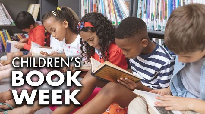 Children sitting on a library floor reading books.