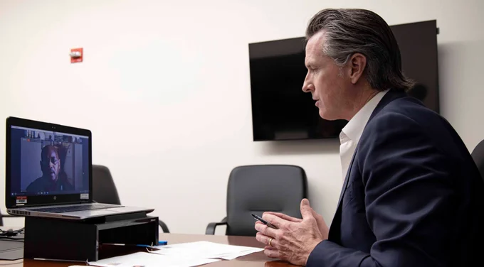 Photograph of Governor Gavin Newsom sitting at a table while on a Zoom call on a laptop with small business owners and members of this task force.