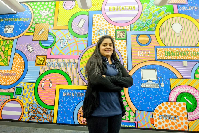 Dipannita Saha, a senior graphic design major, displays the brilliantly, colorful mural that she created for the center.