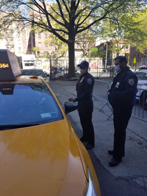 TLC officers manage the line at a food distribution site. There is a yellow taxi in the photo left-center.