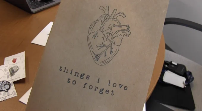 An outline of an anatomical heart is drawn on a notebook. Underneath are the words "things I love to forget."