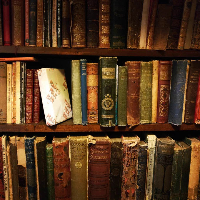 Old books on a shelf, one wrapped box of caramels in the middle