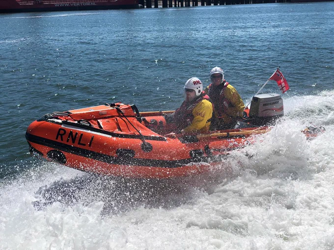 Two crew members aboard Sheerness lifeboat station's inshore lifeboat in sunny conditions powerful through the wake of another boat