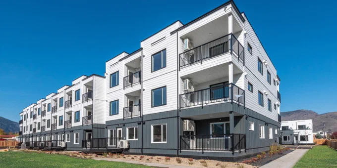 Angled view of new, white and gray, three-storey modular residential building 