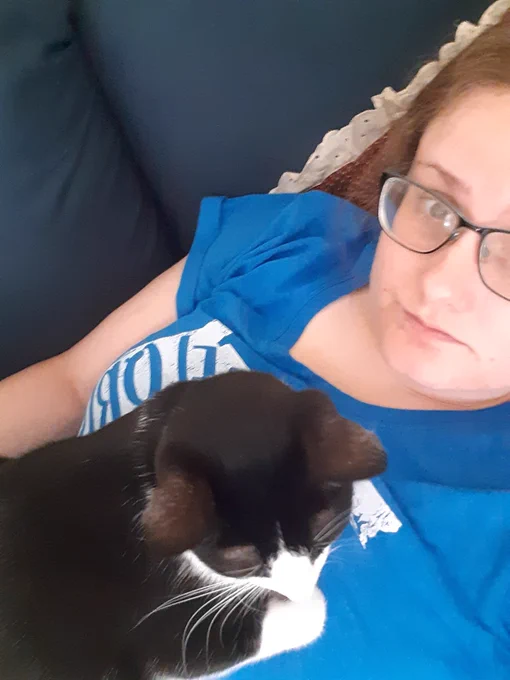 Mandy lies on her sofa with her cat sitting on her chest.