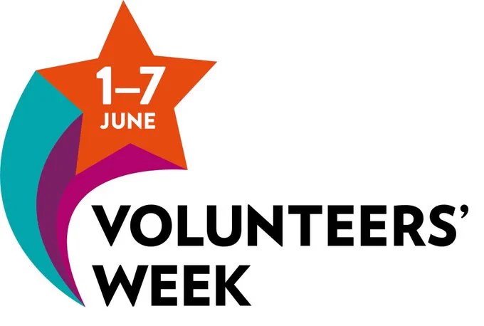 A sign reading volunteers' week in black text. To the top right of the sign there is a red star with 1-7 June written in white text, from the bottom of the star are two lines, one blue and one purple.
