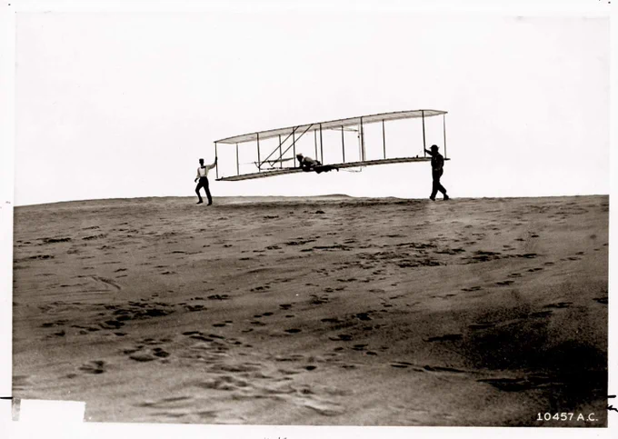 Two men stand next to glider; one man at the controls.