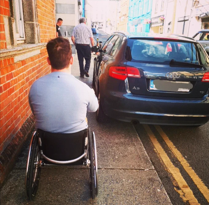 Car parked on double yellow lines on a narrow path with Mike wheeling up to it
