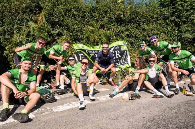 University of Exeter cyclists sat in front of flag