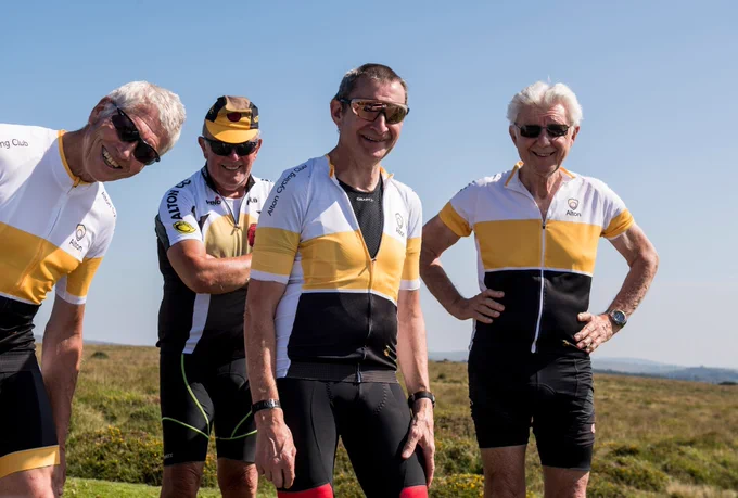  group of cyclists smiling at the camera waiting for the peloton to arrive 