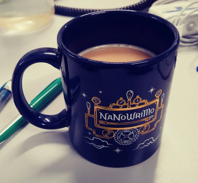 Coffee mug that reads "NaNoWriMo", on a desk.