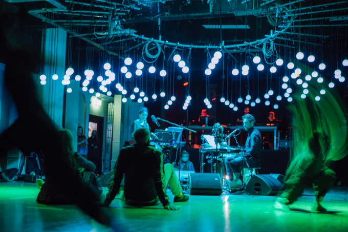 Musicians are in the centre of a circle of orbs performing as blue and green light glows around them