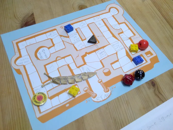 A board game with action fields drawn in, a D6 dice and a D20 dice, Lego blocks and various random objects as pawns