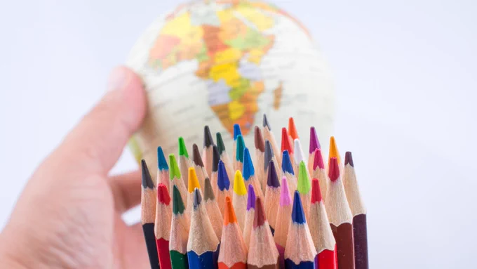 a hand holding a small globe and multicolored pencils.