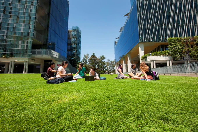 QUT students sit on green grass with computers at Gardens Point