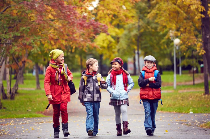 Small group of children walking to school together with a fall background