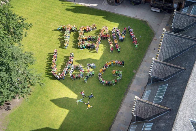 Students on the grass on campus spelling out the letters Team UofG