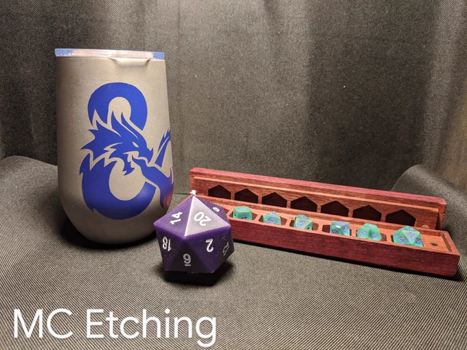 Photo of prizes. Reverse etched stainless steel wine tumbler with a D&D ampersand. D20 shaped candle. Purpleheart wood dice vault containing a set of seafoam green gaming dice.