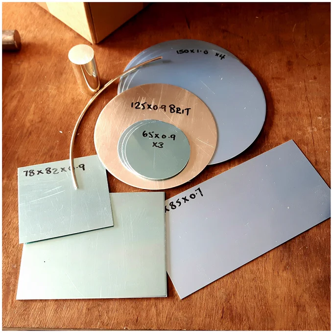 Discs and sheets of silver with wire and bar on a workbench ready for making new work.