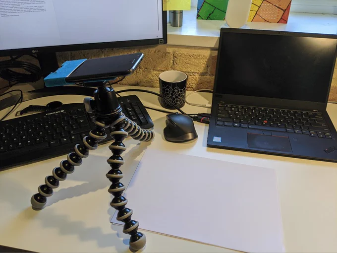 Daniel Hugenroth's DIY visualiser setup using a smartphone strapped to a basic tripod, with the camera facing a blank page on the desk.