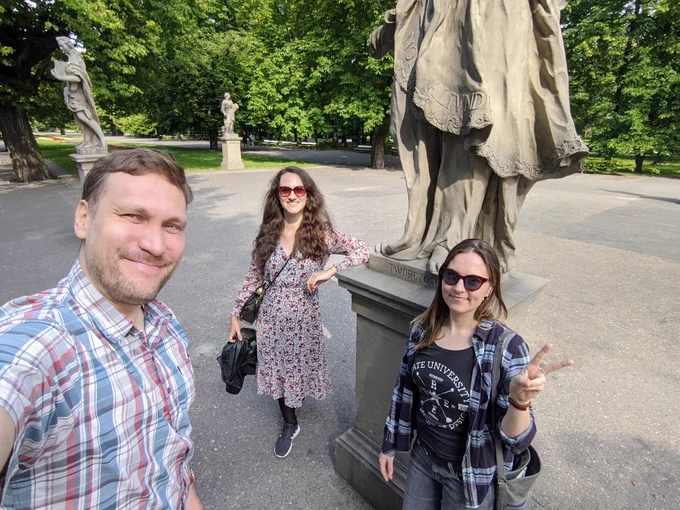 Kamil Brzeziński, Ela Mościcka and Inez Górska-Brzezińska standing under the statue in the park smiling and keeping social distancing
