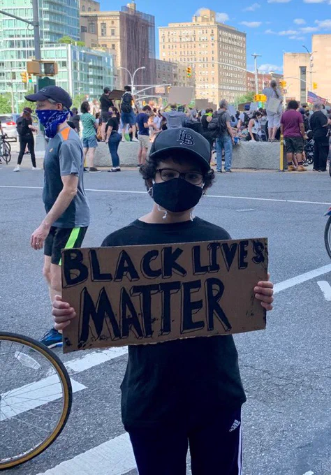 A masked child holding a BLM sign across the street from a protest in Brooklyn’s Grand Army Plaza.