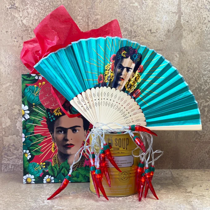 Image shows a bright blue silk fan with an image of Frida Kahlo on it and Frida Kahlo gift bag in the background