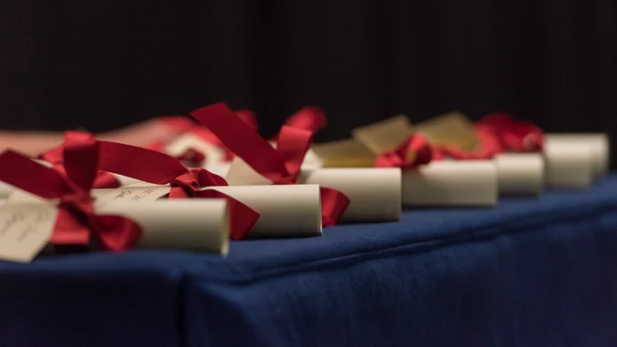 Certificates from the 2019 Pilkington Prize Ceremony tied with red ribbon and lined up on a table with a blue covering.
