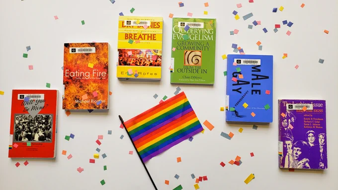 Photos of books in every colour of the rainbow, arranged in a rainbow alongside a Pride flag. 